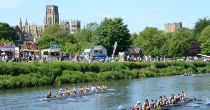 View of Durham Regatta with rowing boats in the river wear, fairground rides and Durham Cathedral in background.